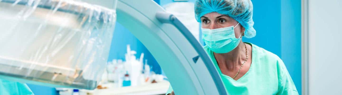 Medical assistant in the operating room verifying orthopedic surgeons work on a human spine, with the help of a c- arm fluoroscope